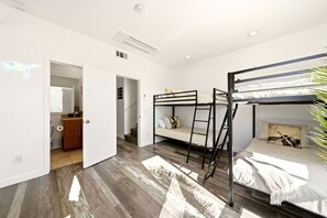 Une chambre avec des lits superposés, un plancher en bois, une armoire et une porte donnant sur une salle de bain.
