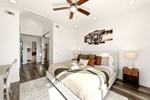 Ein modernes Schlafzimmer mit einem großen Bett, einem Deckenventilator und einem an der Wand befestigten Kunstwerk.