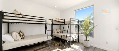 Un dormitorio moderno con literas, un ventanal grande y una planta en maceta.