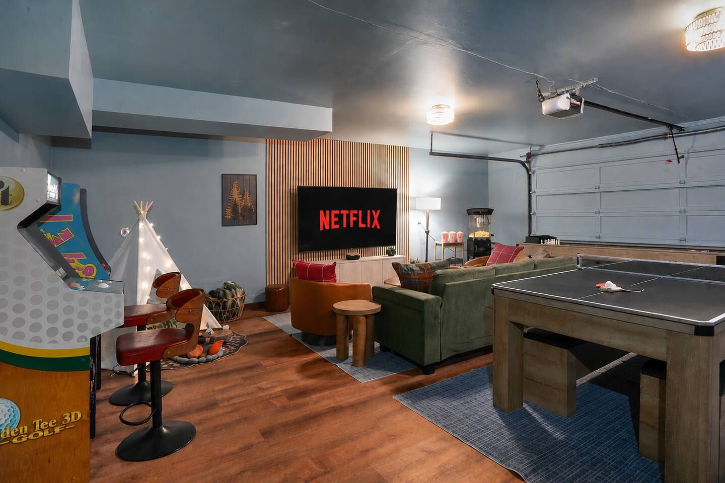 Ein Zimmer mit einem Tischtennis-Tisch, einer Couch, einem Fernseher, der 'NETFLIX' zeigt, und einem kleinen Tisch mit Snacks.
