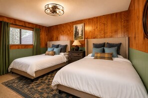 A room with two beds, a wooden paneled wall, a window with curtains, a lamp, and a rug. - Cabin vibe & Lux comfort, Sauna~Hot Tub~Game Room~Fire Pit~Pet friendly (Big Bear Lake)