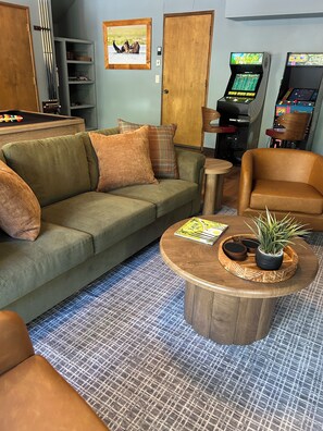 Habitación con mesa de billar, sofá, mesa de centro con planta y juegos de arcade.