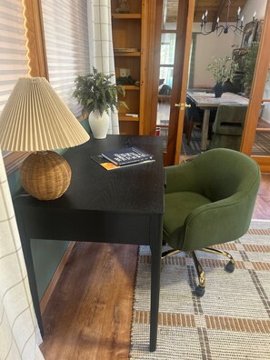 Una habitación con una mesa negra, una silla verde, una lámpara, una planta en maceta y un libro titulado '100 Things to See in the Night Sky'.