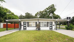 Ein eingeschossiges Haus mit überdachter Veranda, Vorgarten und rotem Zaun.