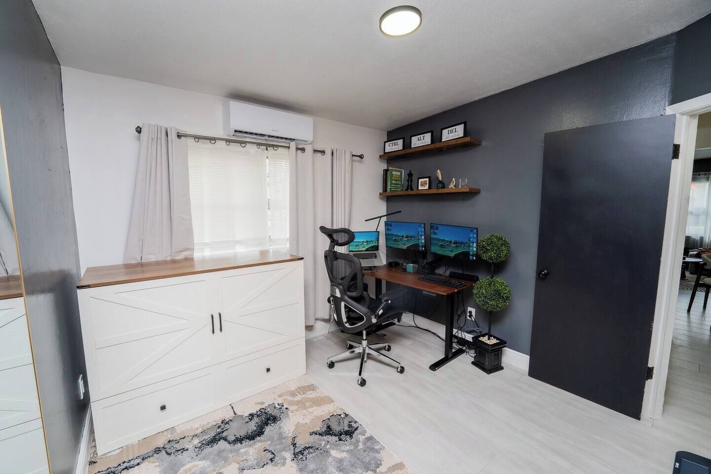 Un espacio de oficina moderno con un escritorio, dos monitores, una silla y una planta pequeña.