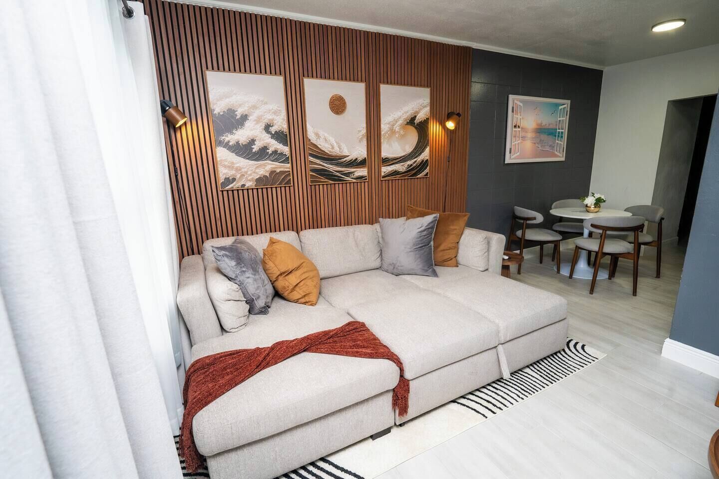 En moderne stue med sofa, puder, et pled og kunst på væggen.