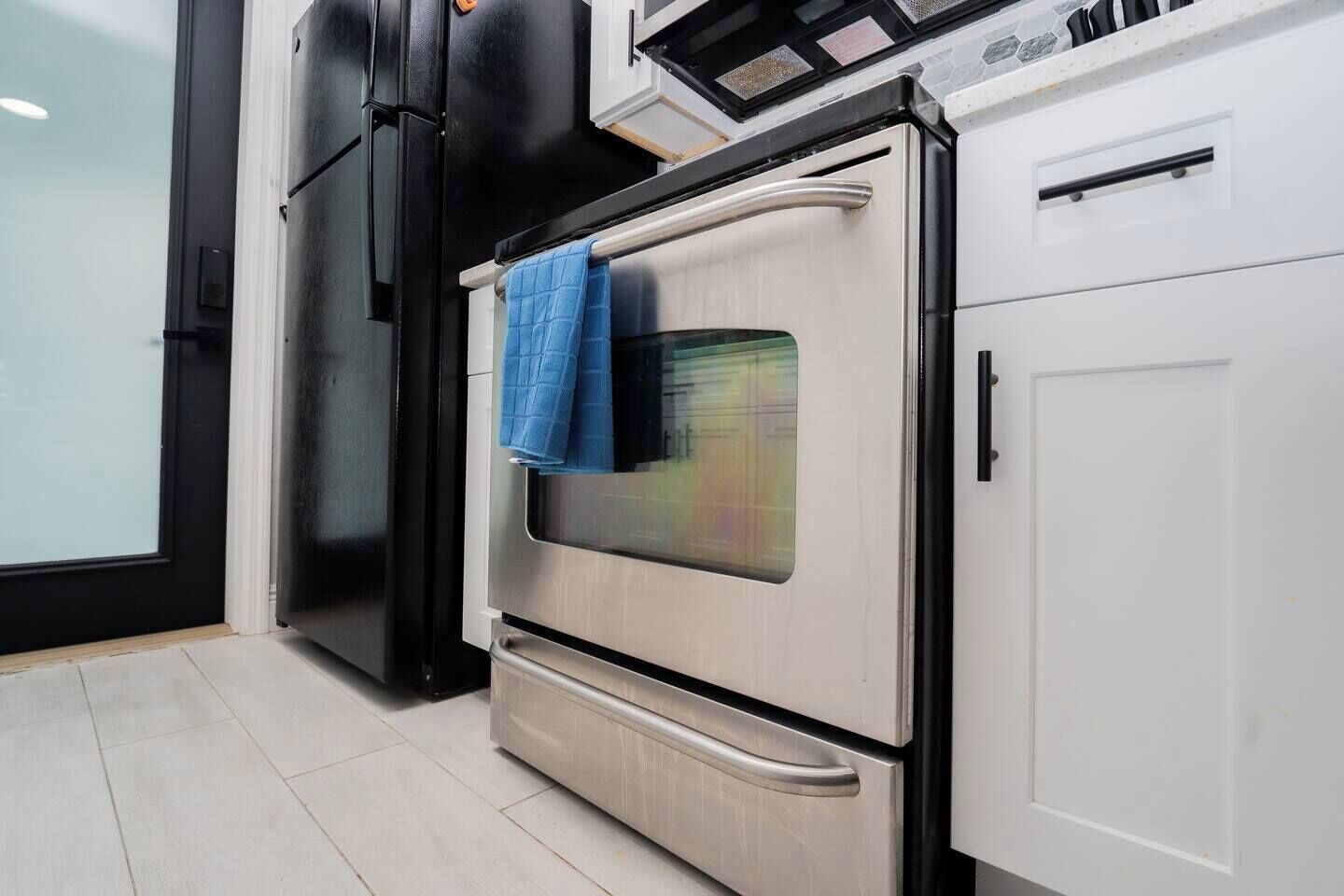 Una cocina con horno de acero inoxidable, refrigerador negro y armarios blancos.