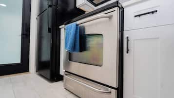 Una cocina con horno de acero inoxidable, refrigerador negro y armarios blancos.