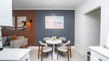 A modern kitchen with a dining area, featuring a white countertop, wooden cabinets, and a round table with chairs.