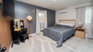 Ein modernes Schlafzimmer mit Bett, Nachttischen, einem Schminktisch mit Spiegel und einer Klimaanlage.
