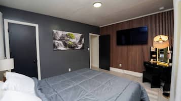 Un dormitorio con cama, televisor montado en la pared, escritorio con lámpara y un cuadro.