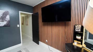 A modern living room with a flat-screen TV mounted on a wooden wall, a door leading to another room, and a small table with decorative items.
