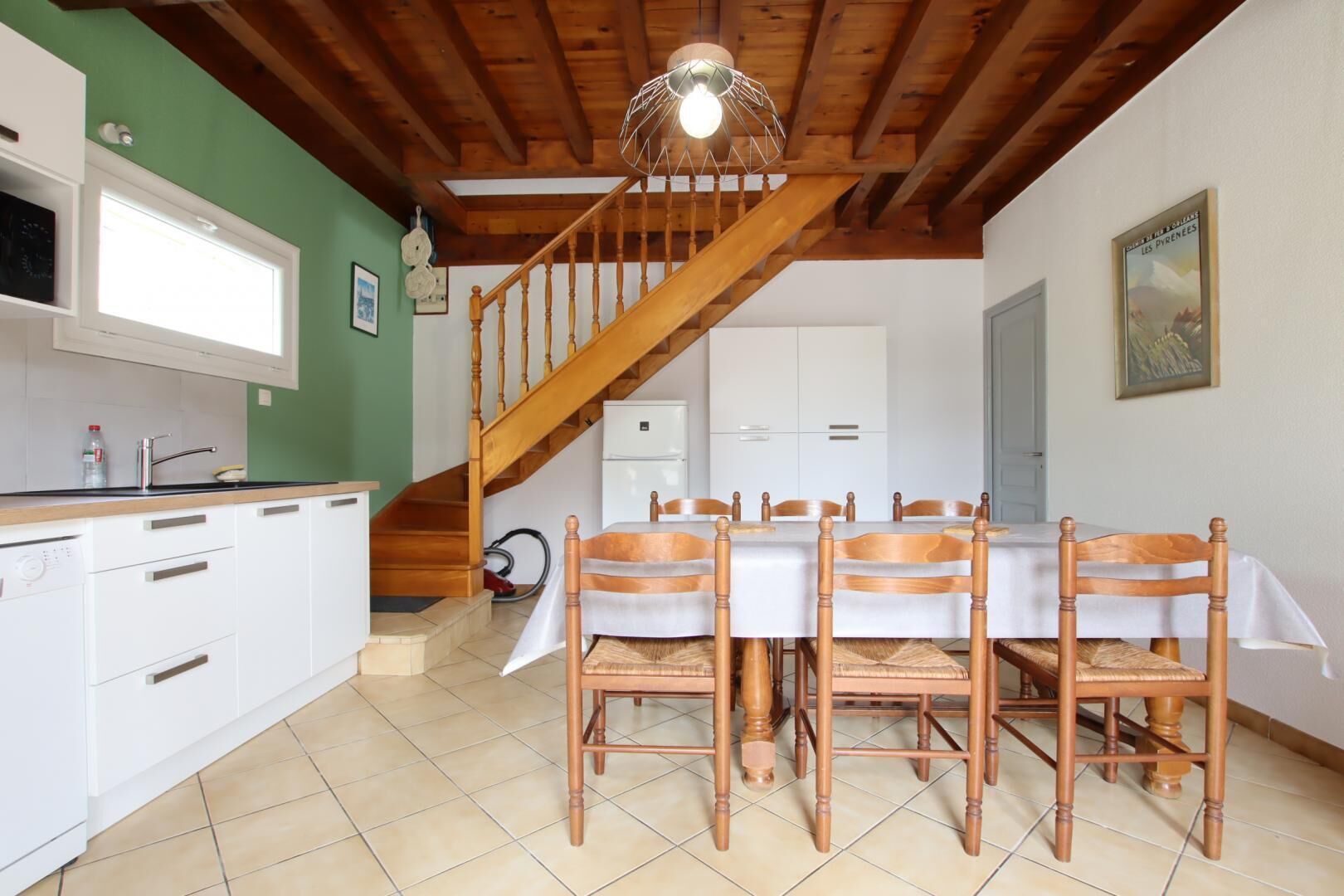 A dining area with a wooden table and chairs, a kitchen with white cabinets, and a staircase leading to another level.