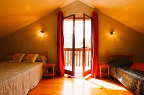Ein Schlafzimmer mit zwei Betten, Holzboden und einer Schiebetür zu einem Außenbereich.