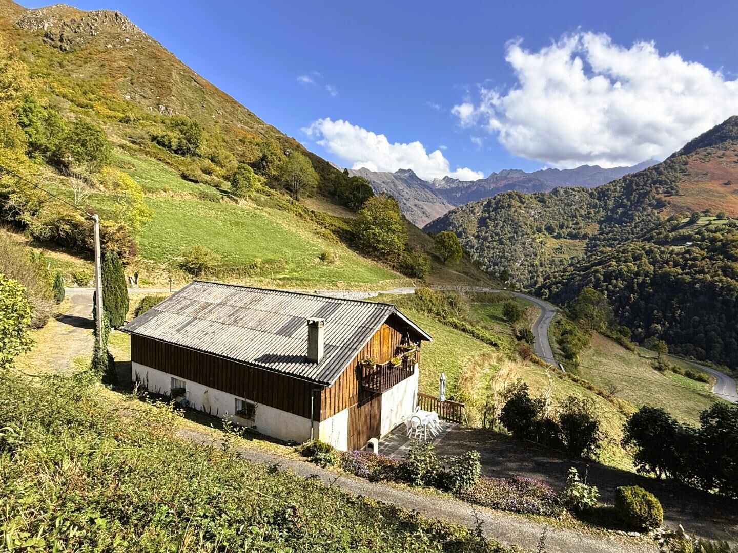 A wooden cabin with a sloped roof, surrounded by a lush green valley and mountains in the background.