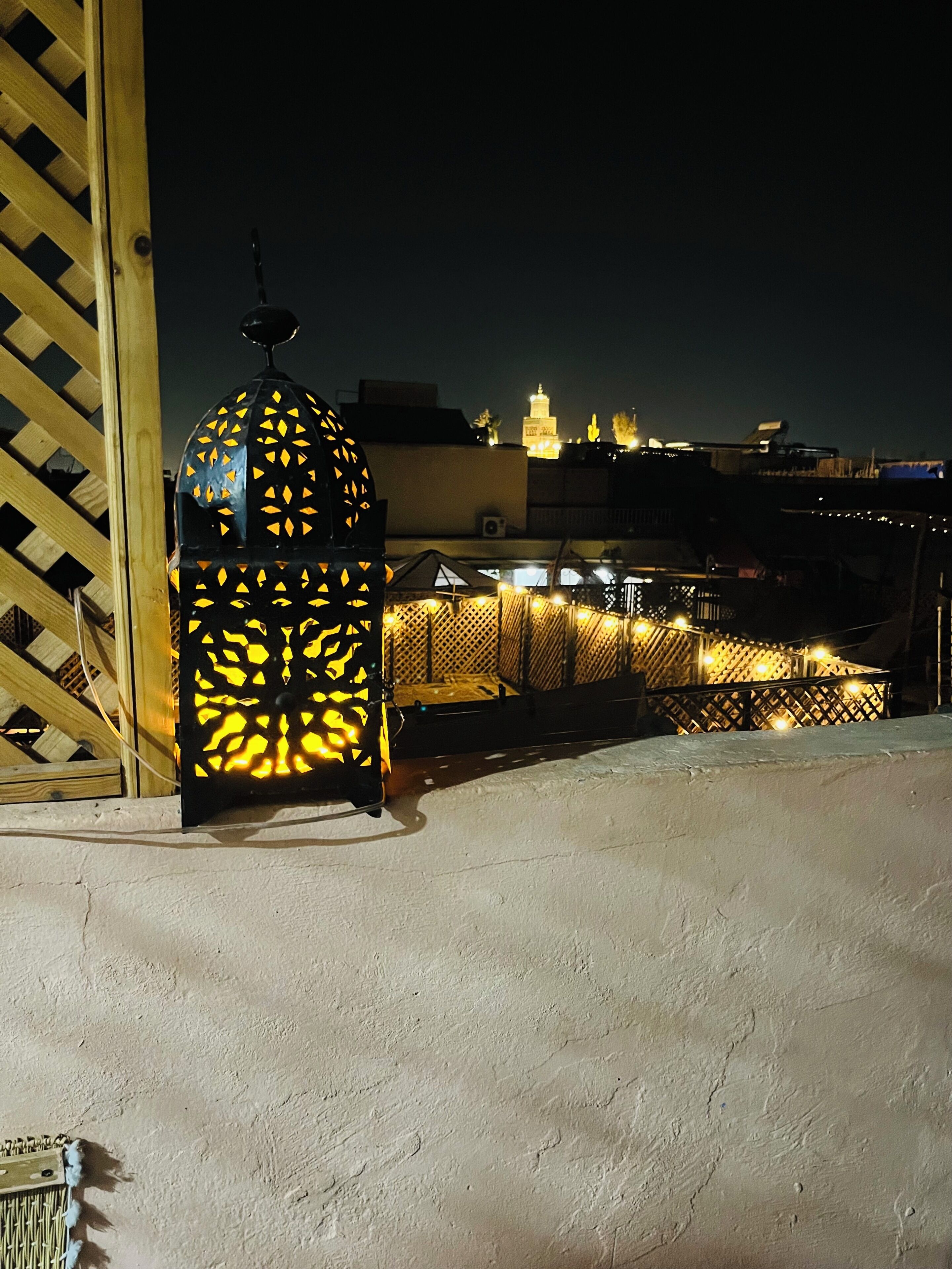 A night scene with a lit lantern, a wooden lattice structure, and a distant illuminated building.