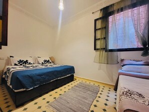 Ein Schlafzimmer mit einem Bett, einem zusätzlichen Bett, einem Fenster mit Vorhängen und einem gemusterten Teppich.