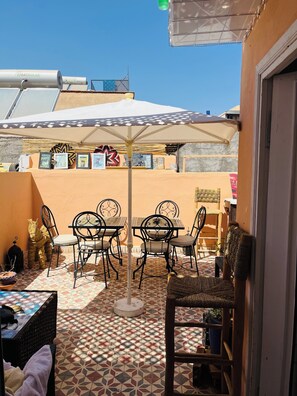 Ein Patio mit Gartenmöbeln, einem Tisch mit weißem Sonnenschirm und Kunstwerken an der Wand.