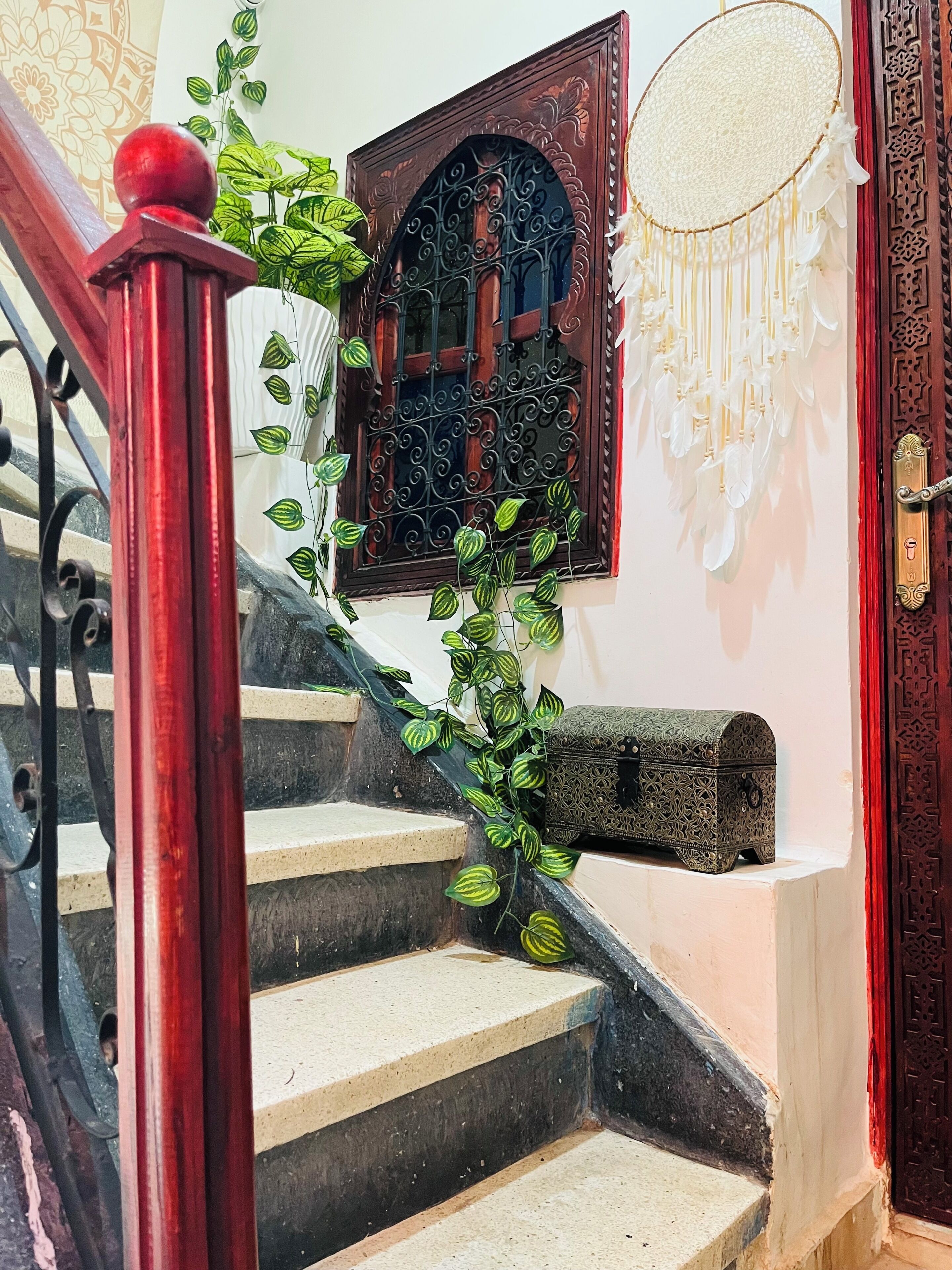 A staircase with a red handrail, a decorative door with intricate carvings, and a window with ornate metal bars.