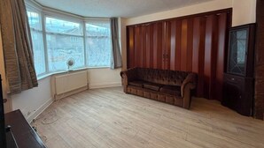 Una habitación con piso de madera, un sofá marrón, un radiador, una ventana con cortinas y un televisor.
