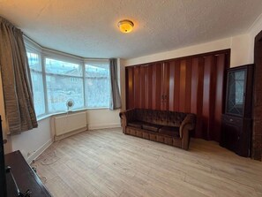 A room with a wooden floor, a brown sofa, a radiator, a window with curtains, and a television. - Ashford Luxury 4-bed Apartment (Ashford)