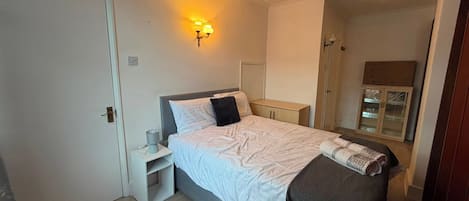 A bedroom with a bed, bedside table, nightstand, and a wall-mounted light fixture.