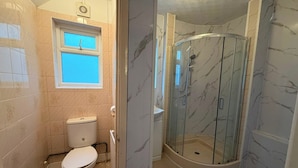 Un baño con inodoro, cabina de ducha y ventana.