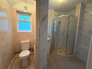 A bathroom with a toilet, a shower enclosure, and a window. - Ashford Luxury 4-bed Apartment (Ashford)