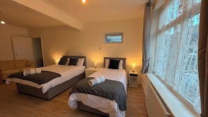 Habitación de hotel con dos camas, una ventana con cortinas de encaje y un radiador.