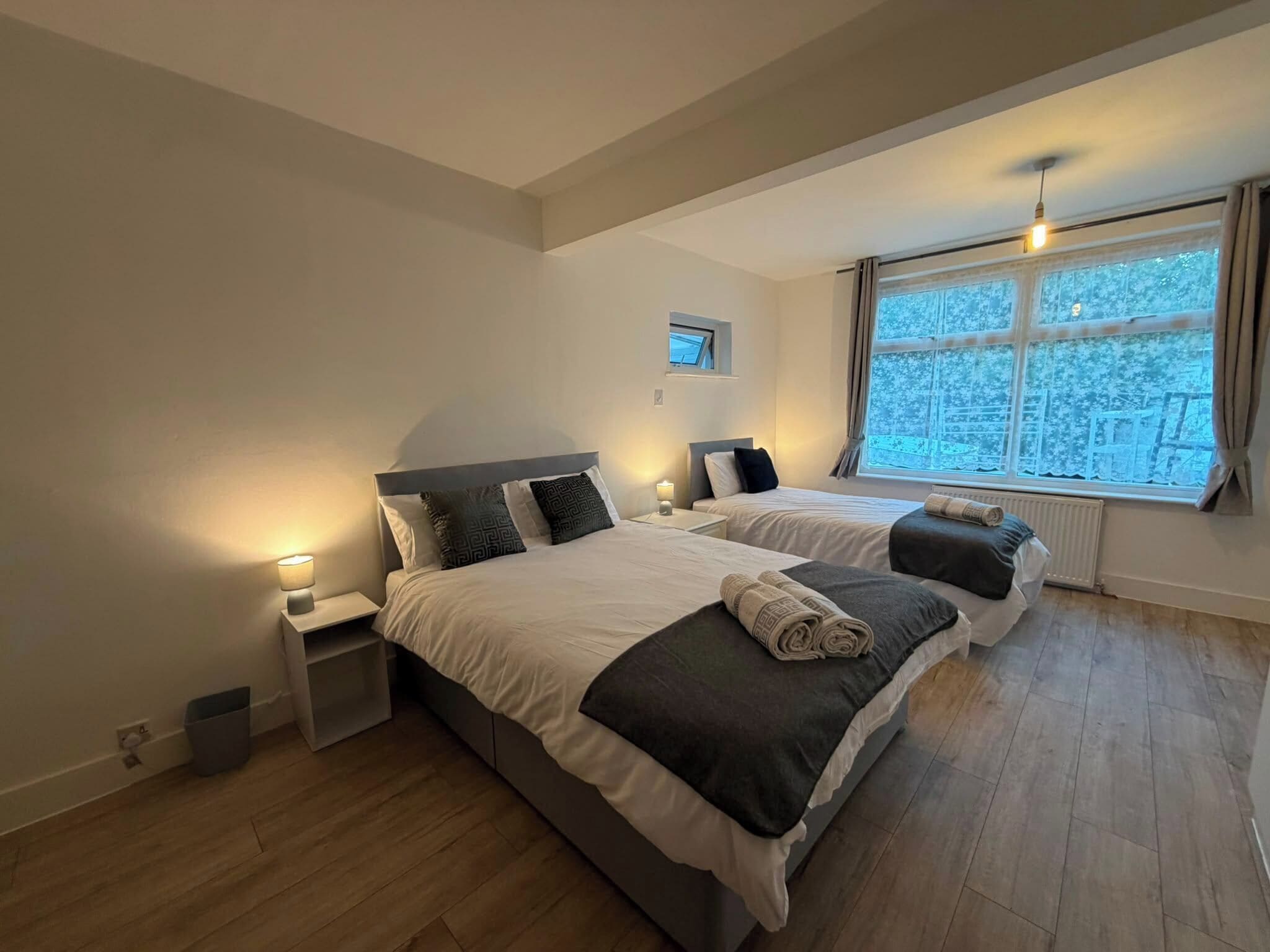 A double bed with a headboard, bedside tables with lamps, a window with curtains, and a view of trees.