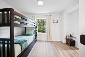 Un dormitori amb un llit superposat, una finestra amb cortines, una petita taula de nit amb una làmpada, i un quadre a la paret.