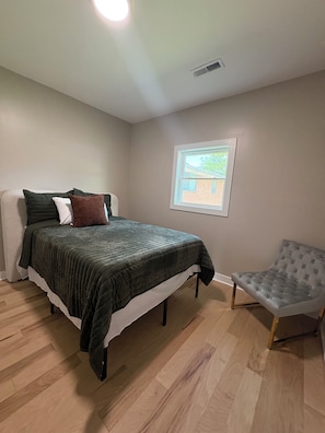 Un dormitorio con cama, una silla, un ventanal y una rejilla en el techo.