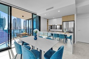 A modern apartment with a dining area, kitchen, and a balcony with a city view. - L14 Luxury 3 Bedroom Apartment with views (Broadbeach)