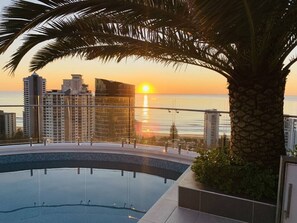 A swimming pool with a sunset view, surrounded by high-rise buildings and palm trees. - L14 Luxury 3 Bedroom Apartment with views (Broadbeach)