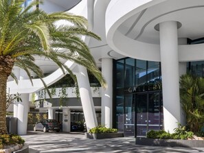 Un edifici modern amb façana corbada, una entrada visible amb la inscripció 'GALLERY' i una palmera al primer pla.