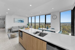 A modern kitchen with a large island, a built-in dishwasher, and a view of the city. - L14 Luxury 3 Bedroom Apartment with views (Broadbeach)
