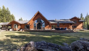 A large, modern log cabin with a prominent glass entryway, a covered patio, and a well-maintained lawn.