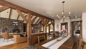 A spacious dining area with a long wooden table, stone fireplace, and exposed wooden beams.