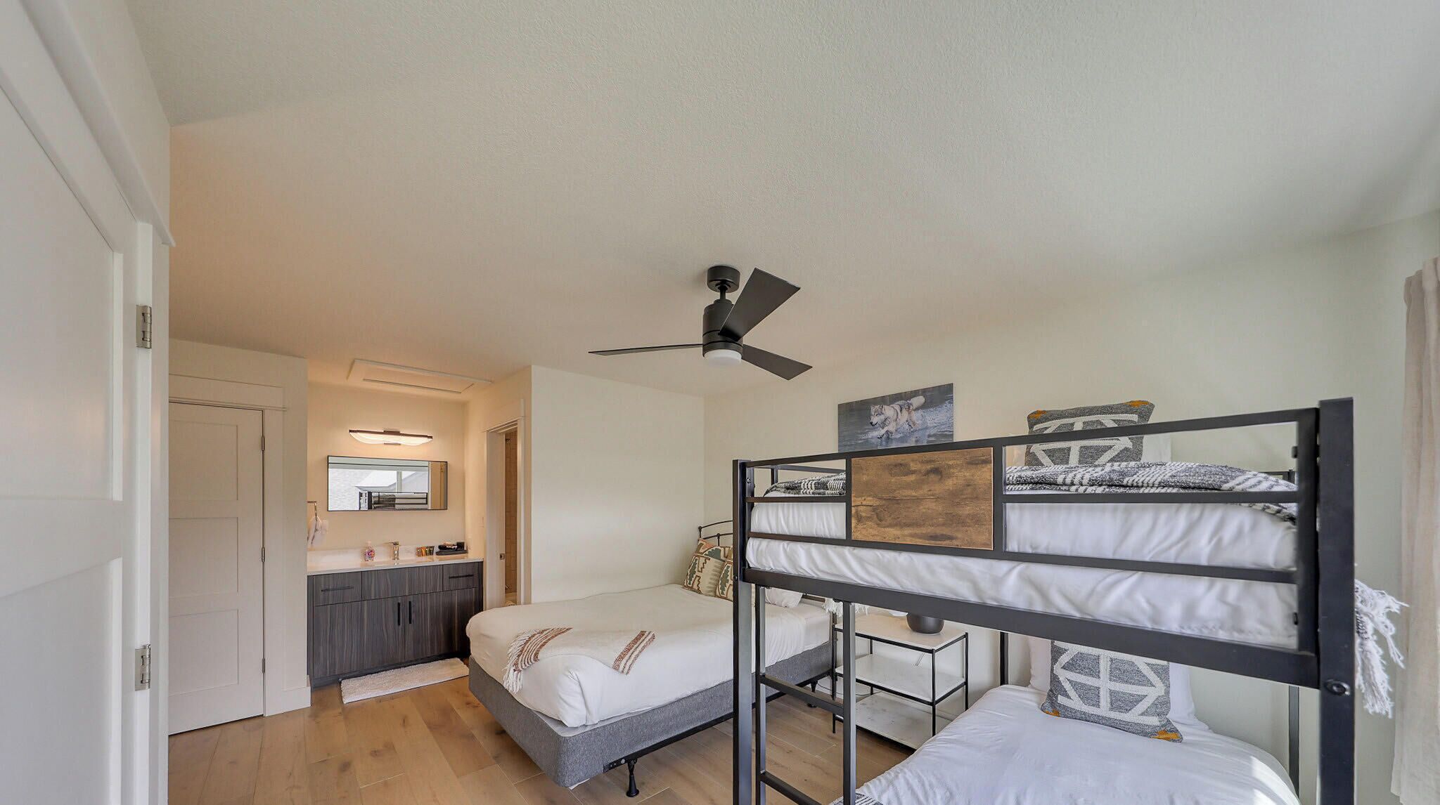Un dormitorio con literas, ventilador de techo, baño pequeño con espejo y piso de madera.