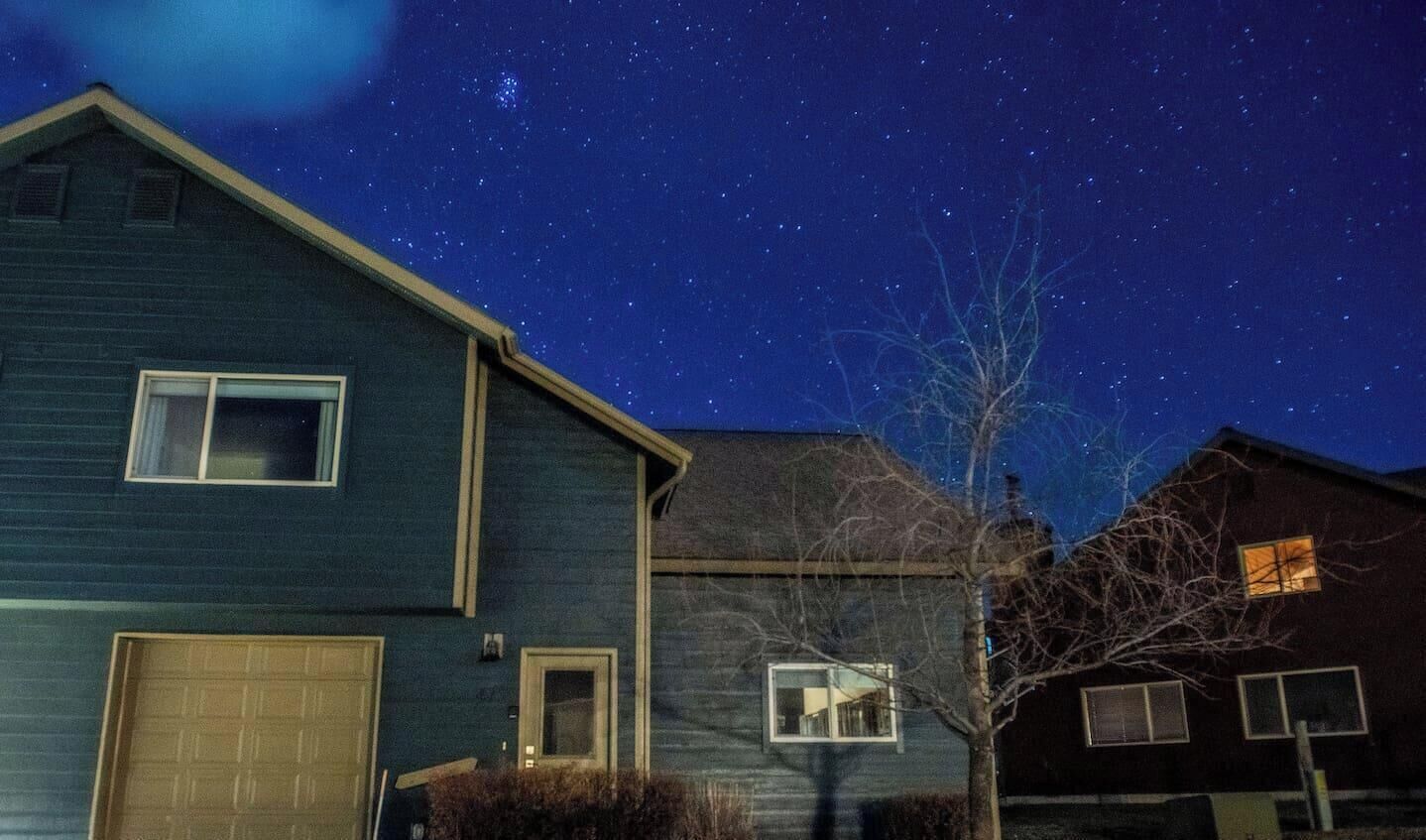 A residential area at night with houses and a clear starry sky.