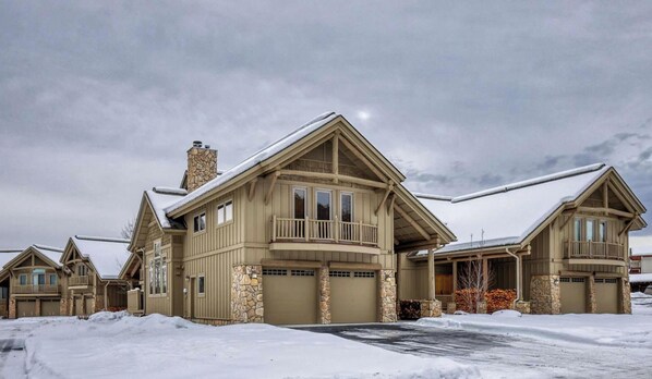 A large, multi-story house with a stone facade, multiple garage doors, and a balcony.