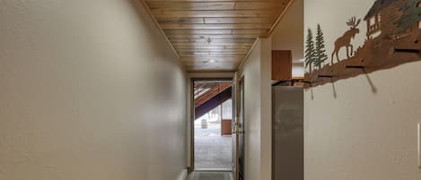 A narrow hallway with wooden ceiling beams, a door leading to an outdoor area, and a wall-mounted decoration of a moose and trees.