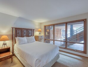 Un dormitorio con una cama grande, dos mesitas de noche con lámparas, un aparador y un ventanal con vistas a una escalera.
