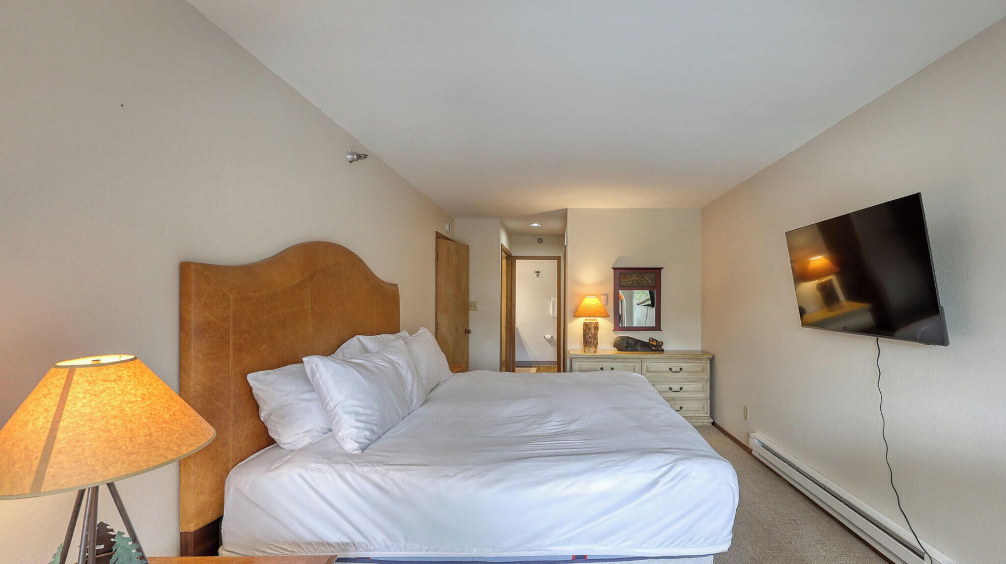 A hotel room with a bed, a bedside lamp, a dresser, a mirror, and a TV mounted on the wall.