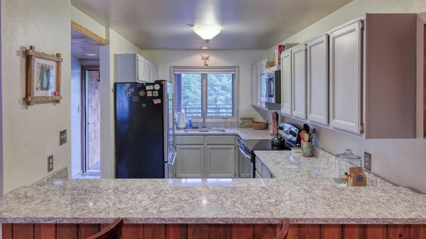A kitchen with granite countertops, white cabinets, a black refrigerator, and a window providing a view of greenery outside.