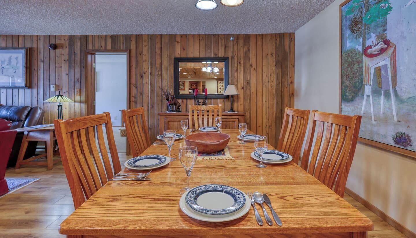 A dining area with a wooden table set for six, surrounded by wooden chairs.