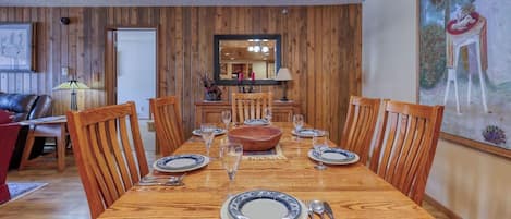 A dining area with a wooden table set for six, surrounded by wooden chairs.