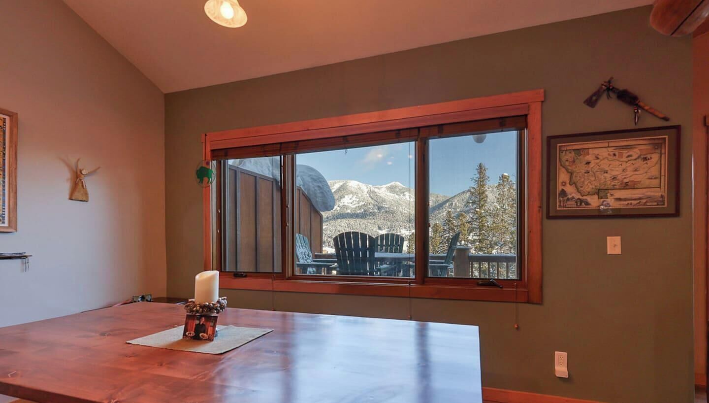 A dining area with a wooden table, a candle, and a window with a view of mountains.
