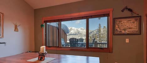 A dining area with a wooden table, a candle, and a window with a view of mountains.