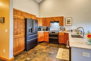 A kitchen with wooden cabinets, a black refrigerator, a stove, and a sink. - Perfect Location! High in the Pines, Hot Tub! (Big Sky)